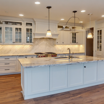 Modern white luxury kitchen with marble island countertops, glass-front cabinets, pendant lighting, and hardwood floors