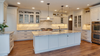 Modern white luxury kitchen with marble island countertops, glass-front cabinets, pendant lighting, and hardwood floors