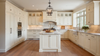 Luxury white farmhouse kitchen with marble countertops, large island, shaker cabinets, pendant lighting, and warm wood floors
