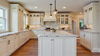 Luxury white farmhouse kitchen with marble island, custom cabinets, pendant lighting, and hardwood floors