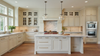 Bright modern white kitchen with marble island, glass pendant lights, custom cabinetry, and stainless steel double ovens