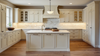 Elegant white shaker-style kitchen with marble countertops, large center island, custom cabinetry, and warm hardwood floors